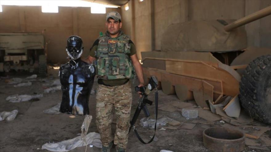 Fuerza iraquí está al lado de un tanque de madera con un maniquí en la mano. 