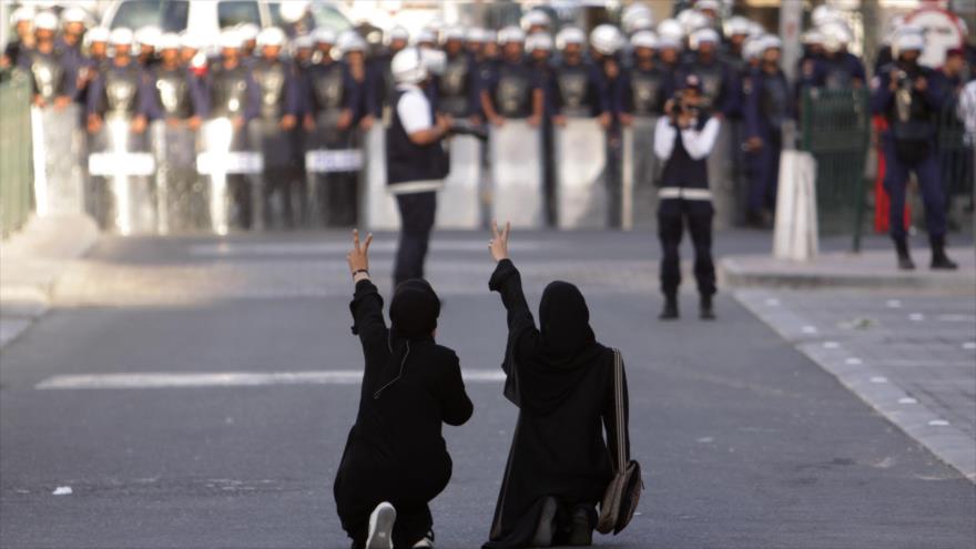 Dos manifestantes antigubernamentales se arrodillan en la calle y hacen gestos hacia la Policía antidisturbios en la capital de Baréin, Manama.