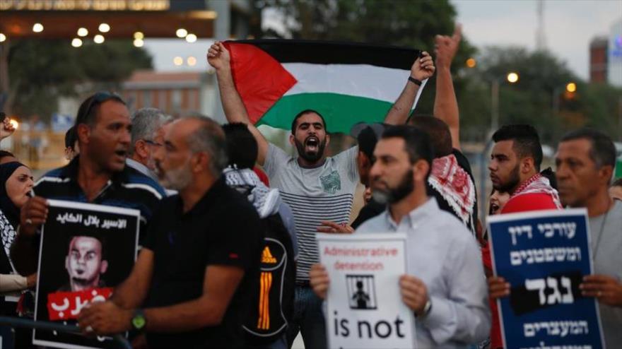 Un manifestante palestino agita su bandera nacional mientras otros sostienen carteles contra la detención administrativa durante una manifestación en apoyo a Bilal Kayedal preso palestino en huelga de hambre, 9 de agosto de 2016.