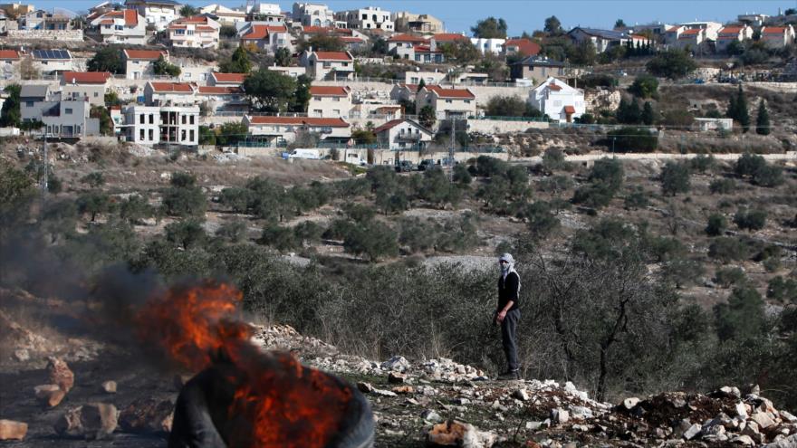 Un palestino mira a los neumáticos en llamas durante un enfrentamiento con las fuerzas de guerra de Israel tras una protesta contra la expropiación de las tierras palestinas por parte del régimen en la aldea de Kfar Qaddum, cerca de la ciudad cisjordana de Nablus, 9 de diciembre de 2016.