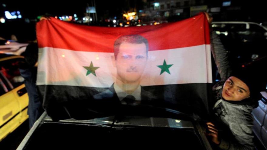 Los ciudadanos sirios llevan una bandera nacional con la foto de su presidente, Bashar al-Asad, mientras celebran la victoria del Ejército sirio contra los grupos armados en Alepo, 12 de diciembre de 2016.