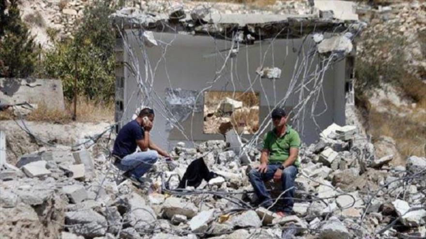 Dos ciudadanos palestinos se sientas en escombros de sus casas en Yabel Mukaber en Al-Quds (Jerusalén), demolidas por las autoridades del régimen israelí.