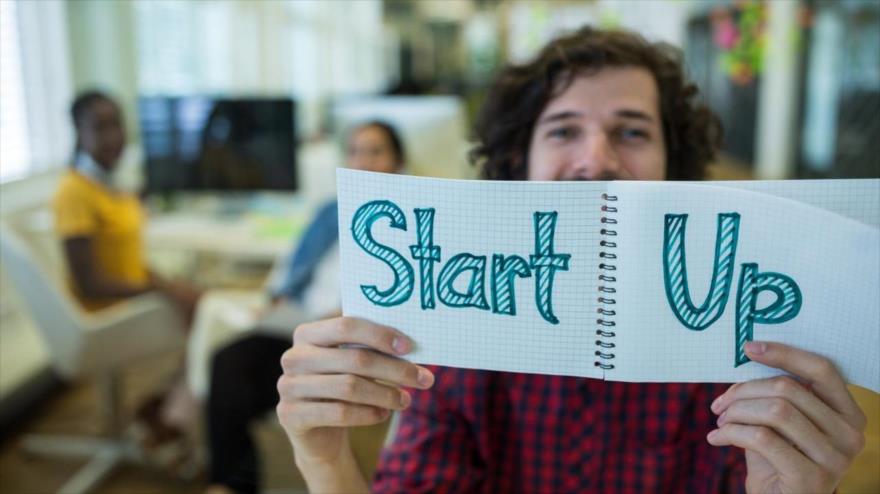 Un joven sostiene un papel en que se lee Start Up, una empresa emergente.