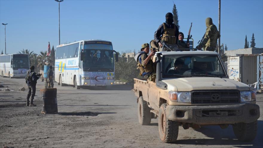 Las fuerzas de la oposición siria cerca de los autobuses que trasladan a los rebeldes sirios evacuados del distrito de Al-Waer, en el norte de Homs, 19 de marzo de 2017.