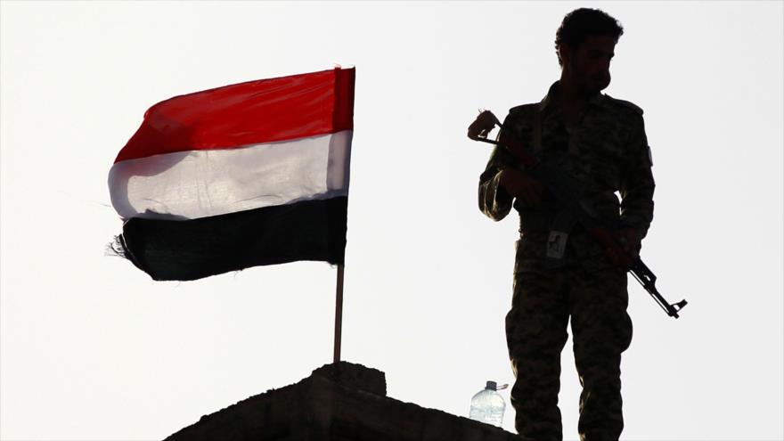 Un miembro del movimiento popular yemení Ansarolá de pie junto a una bandera nacional de Yemen en Saná (capital).