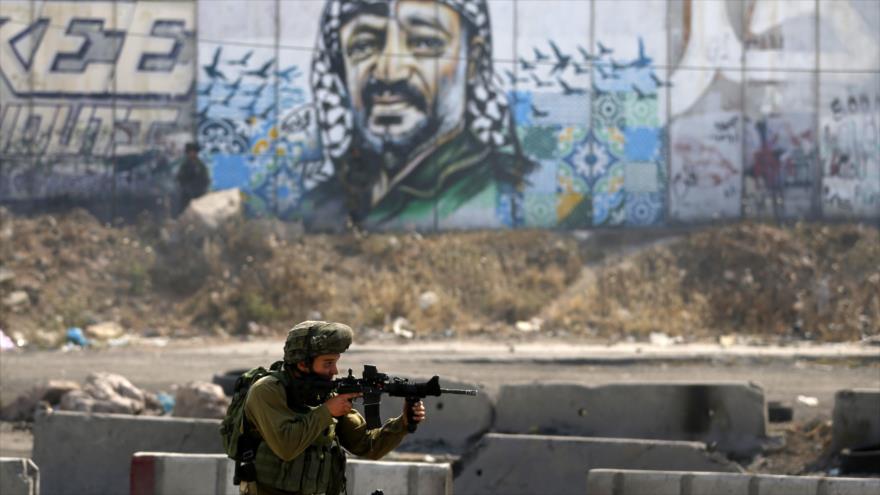 Un soldado israelí toma una posición de alerta frente a un retrato mural del fallecido líder palestino Yaser Arafat durante una protesta de los palestinos. 22 de mayo de 2017
