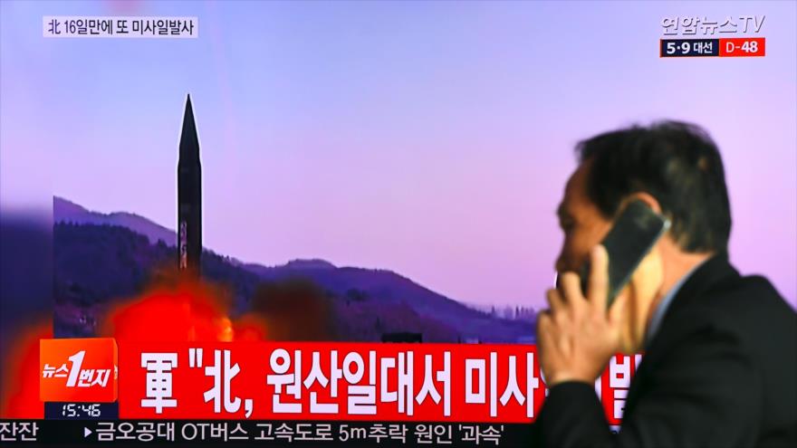 Un hombre hablando por el móvil pasa por delate de una pantalla que muestra una prueba de misil de Corea del Norte.