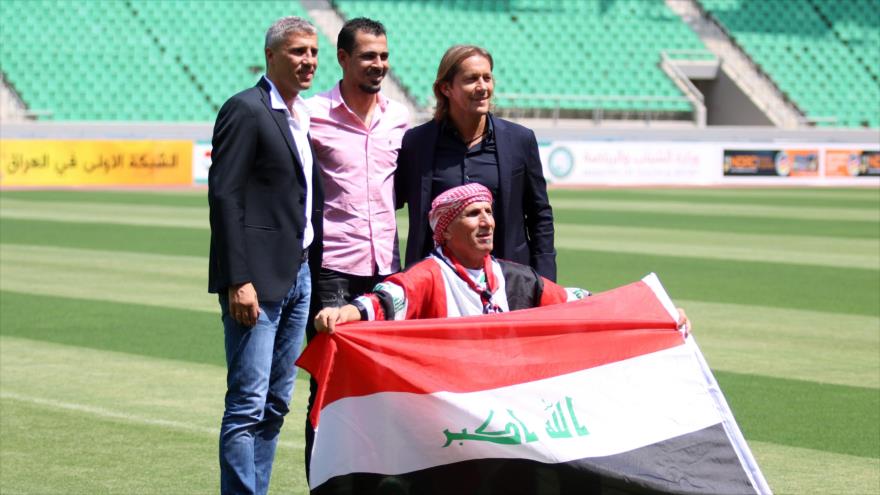 Un ciudadano iraquí extiende la bandera de su país, junto a exfutbolistas, Hernán Crespo (izda.), Yunes Mahmud (centro) y Miquel Salgado.