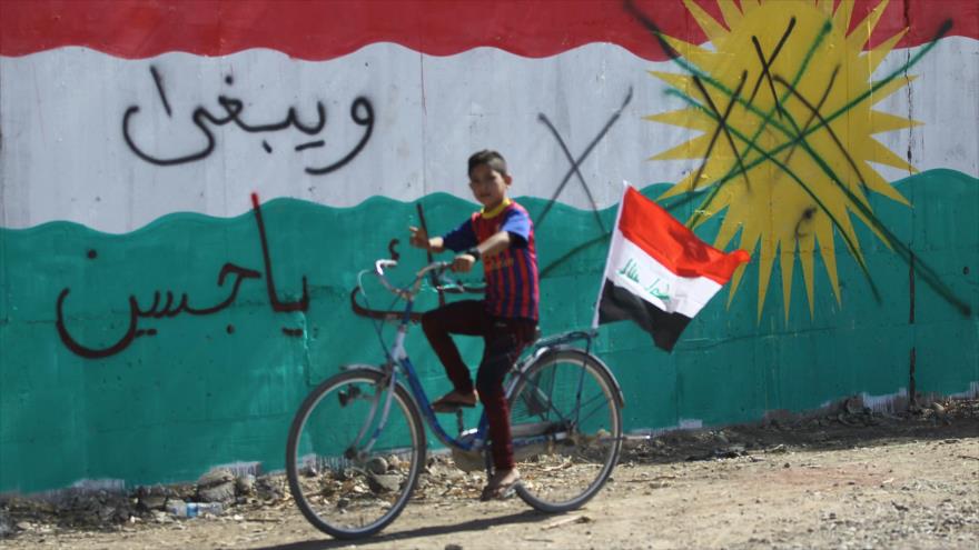 Un niño lleva una bandera nacional iraquí junto a un mural que representa la bandera kurda cerca de Kirkuk, 17 de octubre de 2017.