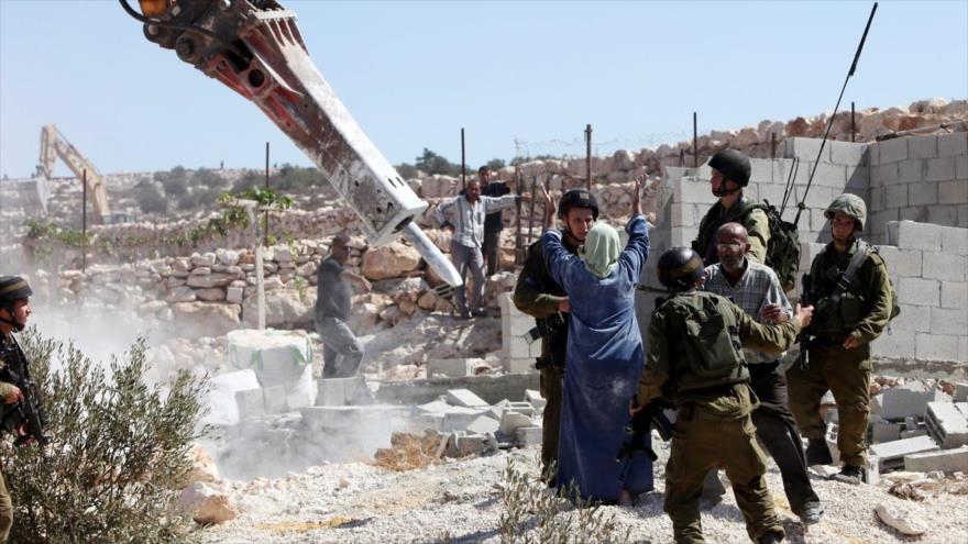 Soldados israelíes impiden que una palestina se acerque y proteste cuando una topadora del regimen israelí demuele su casa.