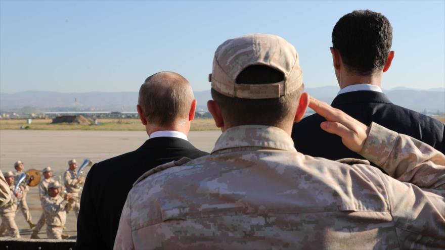 El presidente ruso, Vladimir Putin (izda.), y el presidente de Siria, Bashar al-Asad (dcha.), observan un desfile militar en la base aérea rusa en Hmeimim, 11 de diciembre de 2017.