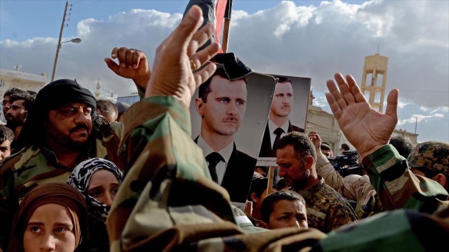Los sirios, portando imágenes de su presidente, celebran la llegada de un convoy militar a un pueblo cerca de la ciudad de Hama, 4 de mayo de 2016.