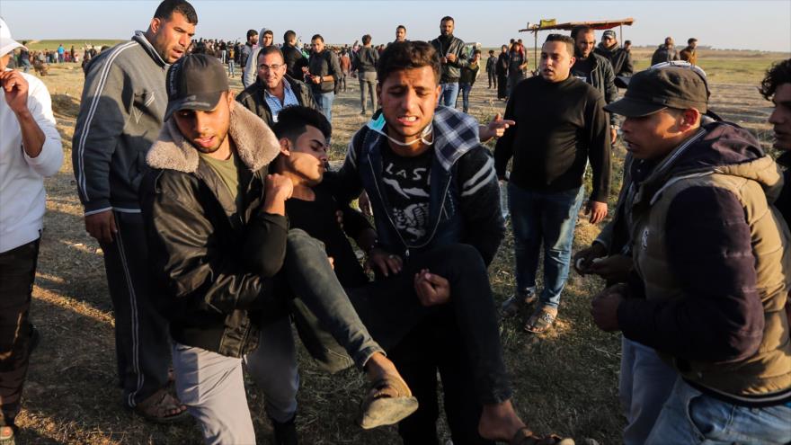 Palestinos llevan en volandas a un joven herido por el régimen israelí durante las protestas en la Franja de Gaza, 31 de marzo de 2018.