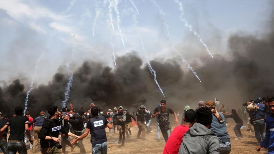 Manifestantes palestinos bajo una lluvia de gas lacrimógeno lanzado por las fuerzas israelíes en Jan Yunis, Franja de Gaza, 27 de abril de 2018.