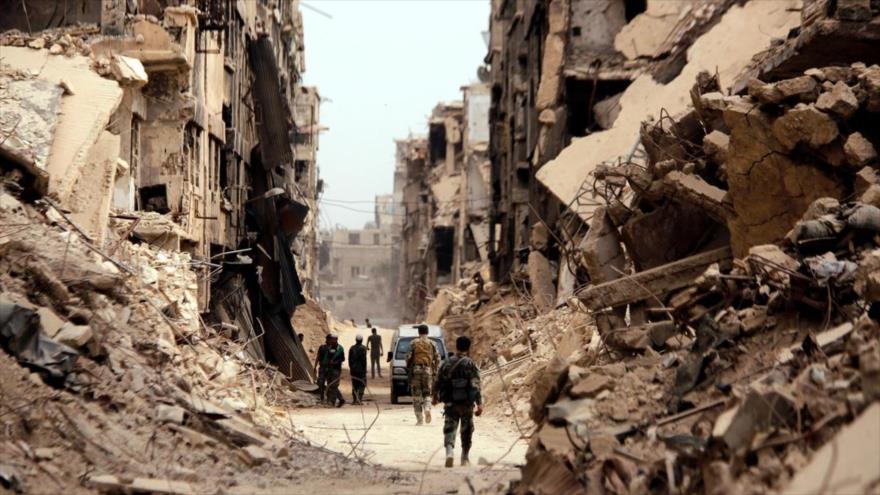 Soldados sirios pasan frente a edificios dañados en el campo de refugiados palestinos de Al-Yarmuk, en el sur de Siria.