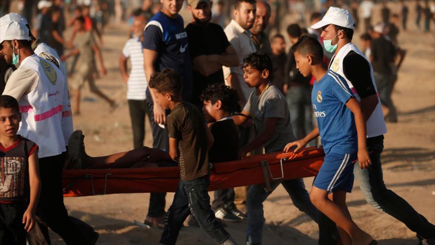 Palestinos trasladan a un adolescente herido durante una protesta realizada en la Franja de Gaza, 27 de julio de 2018.