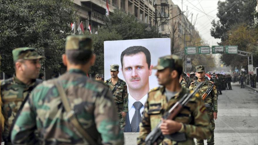 Los soldados sirios pasan frente a un retrato de su presidente Bashar al-Asad durante el aniversario de la retoma de Alepo, 21 de diciembre de 2017.