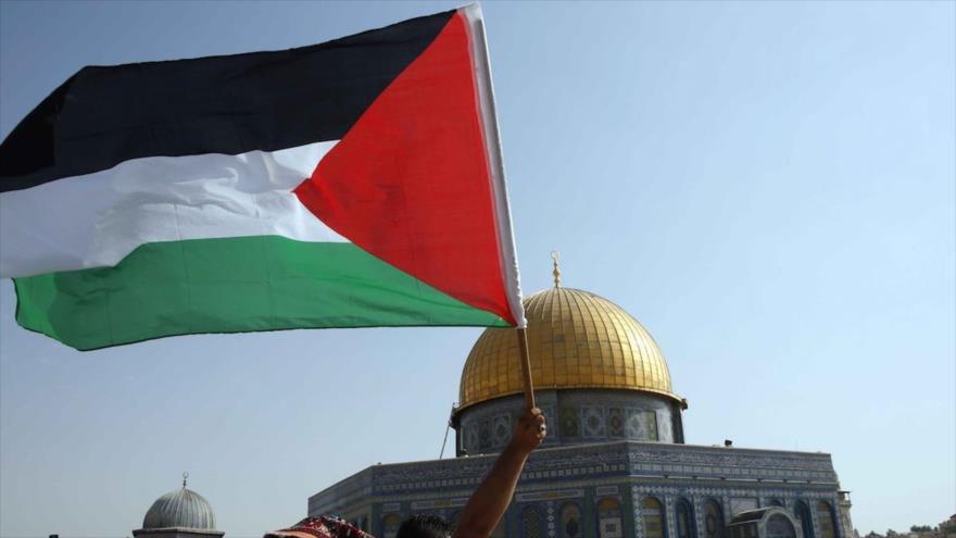 Palestinos ondean su bandera nacional frente a la Cúpula de la Roca en la Explanada de la Mezquita Al-Aqsa, en Al-Quds (Jerusalén).