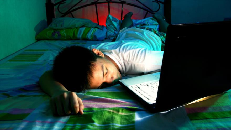 Niño se queda dormido frente a un portatil en su cama.