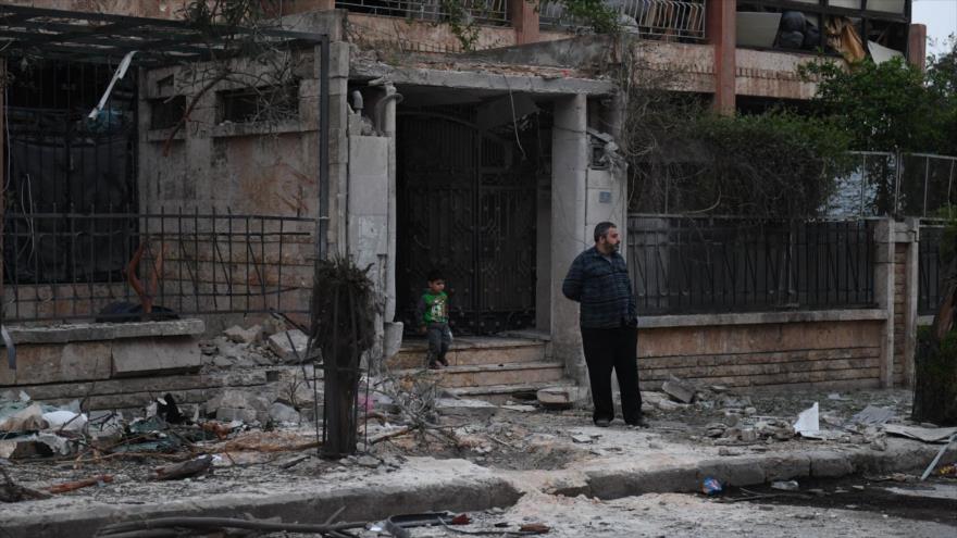 Un hombre y un niño cerca de un edificio alcanzado por un cohete disparado por terroristas en Alepo (Siria), 14 de abril de 2019. (Foto: AFP)