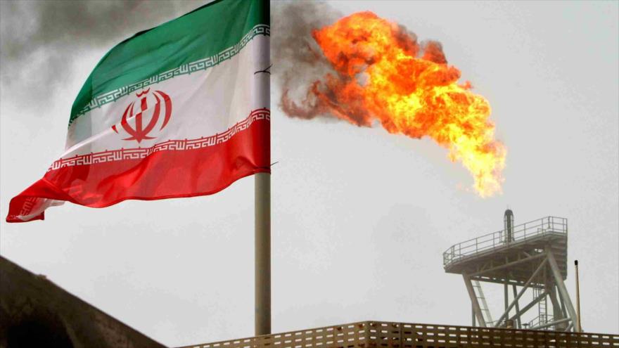 Una bandera nacional iraní, junto a una llama de gas en una plataforma de producción de petróleo.