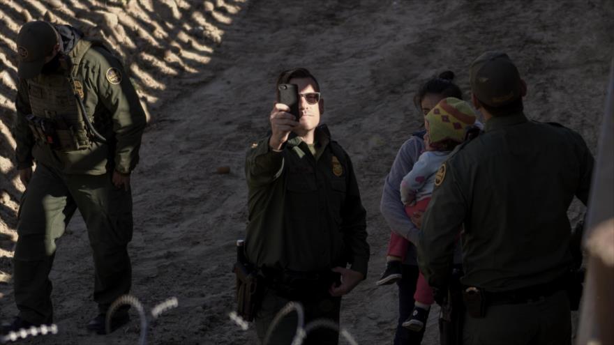 Un agente fronterizo estadounidense toma fotos de un periodista que capturaba con su cámara la detención de migrantes.