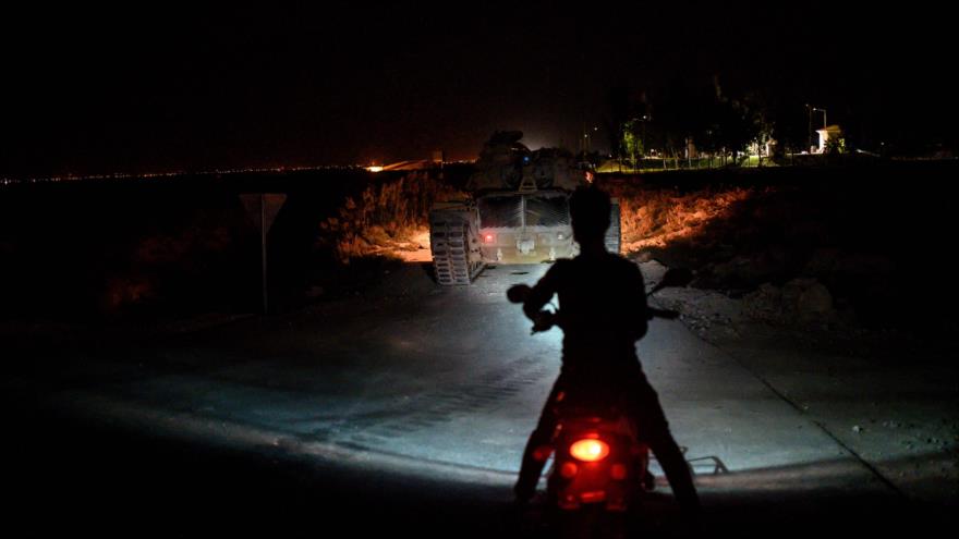 Un motociclista se para en medio de una carretera mientras un tanque turco se acerca a la frontera turco-siria, 8 de octubre de 2019. (Foto: AFP)