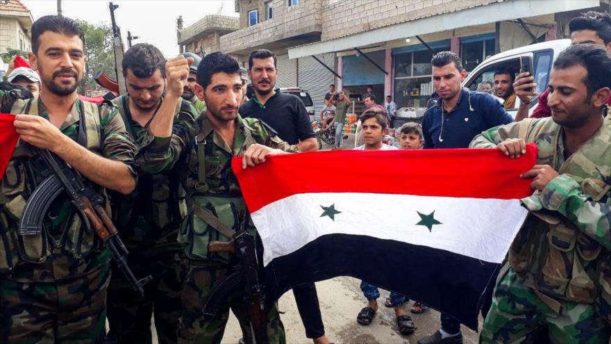 Soldados sirios posan con la bandera nacional en la ciudad de Kobani, en el norte de Siria, 17 de octubre de 2019. (Foto: AFP)