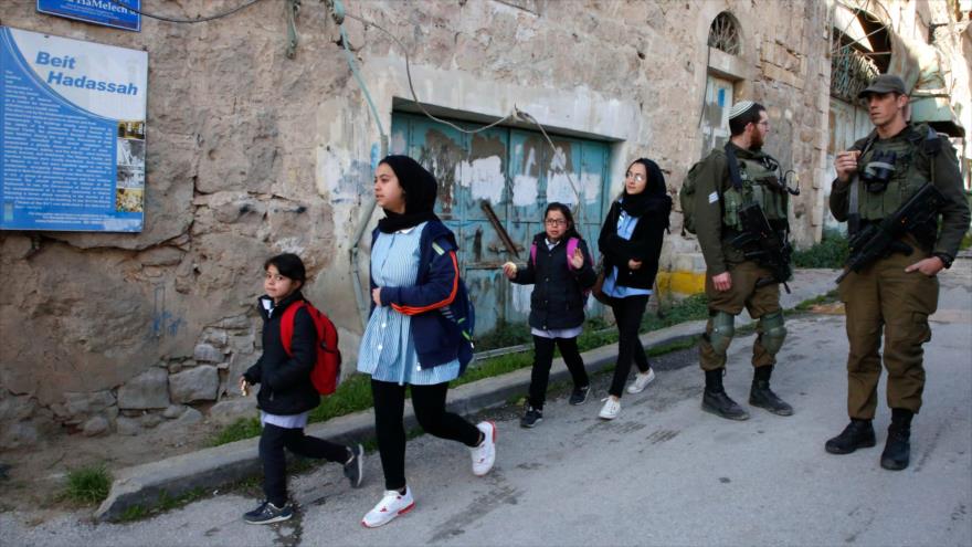 Niños escolares palestinos pasan junto a soldados israelíes en Cisjordania, en los territorios ocupados, 13 de febrero de 2019. (Foto: AFP)