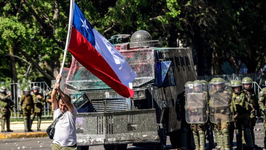 Un manifestante, con la bandera chilena, camina frente a un vehículo policial durante una protesta en Santiago, 28 de octubre de 2019. (Foto: AFP)