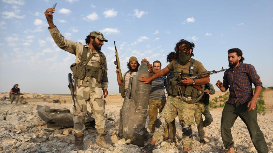 Terroristas de Hayat Tahrir Al-Sham posan para una foto con los restos de un avión de caza sirio derribado en Idlib, el 14 de agosto de 2019.