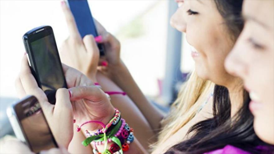 Unas jóvenes interactúan entre sí mientras consultan sus teléfonos móviles.