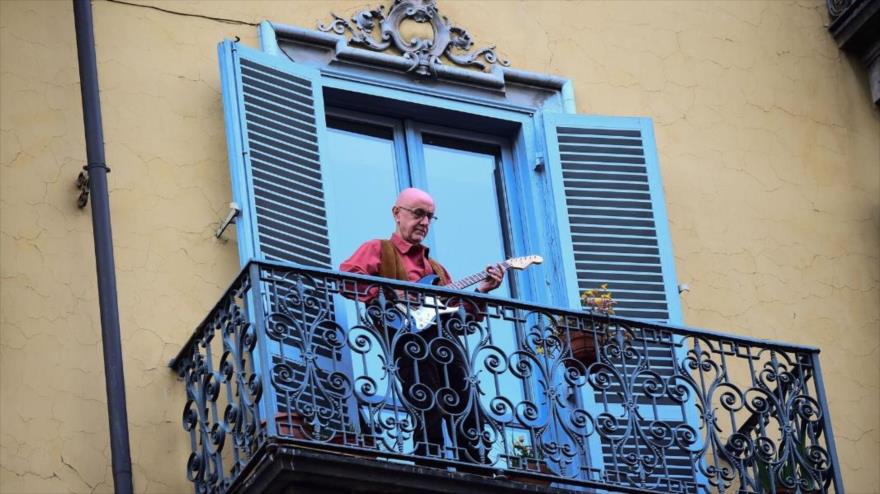 Un hombre toca música desde el balcón de su casa, mientras está en cuarentena para protegerse ante la COVID-19.