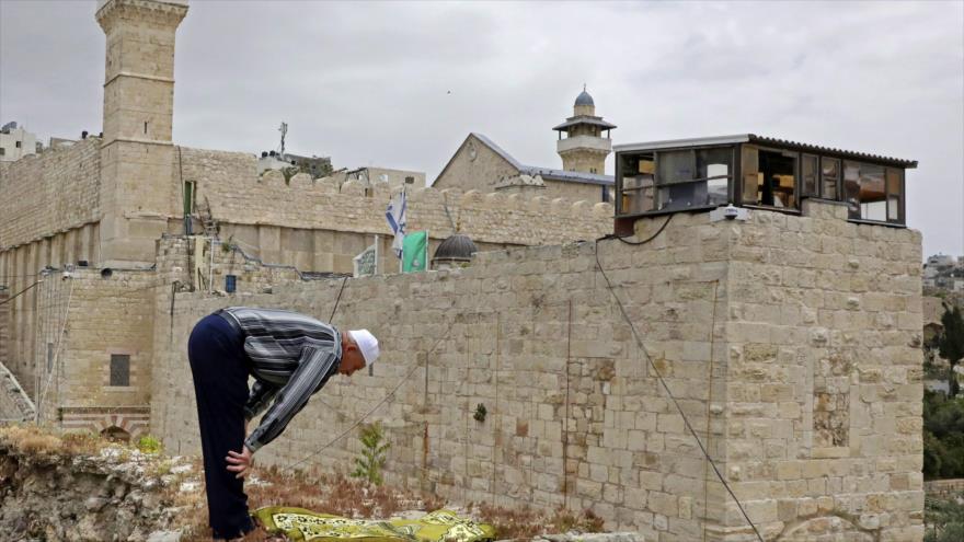 Un palestino reza en la azotea de su casa frente a la Mezquita de Ibrahim en la ciudad cisjordana de Al-Jalil (Hebrón), 24 de abril de 2020. (Foto: AFP)