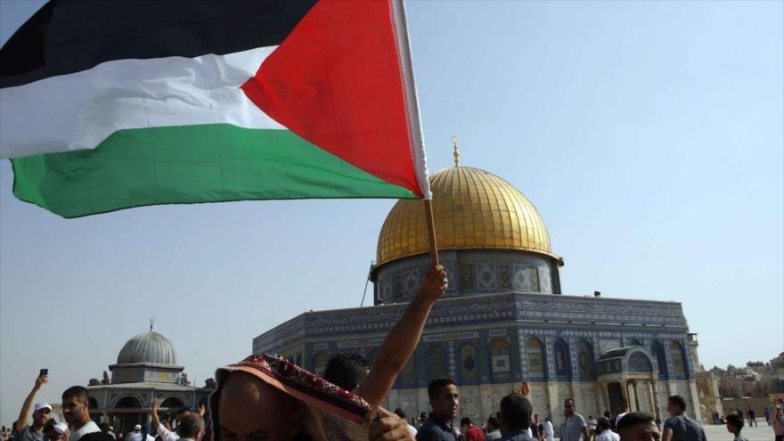 Palestinos ondean su bandera nacional frente a la Cúpula de la Roca en la Explanada de la Mezquita Al-Aqsa, en Al-Quds.