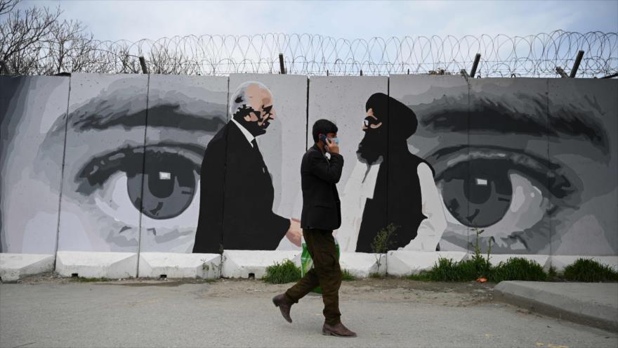 Un hombre pasa frente a una pared con las imágenes de Zalmay Khalilzad (izq.) y Abdul Qani Baradar, en Kabul, 5 de abril de 2020. (Foto: AFP)