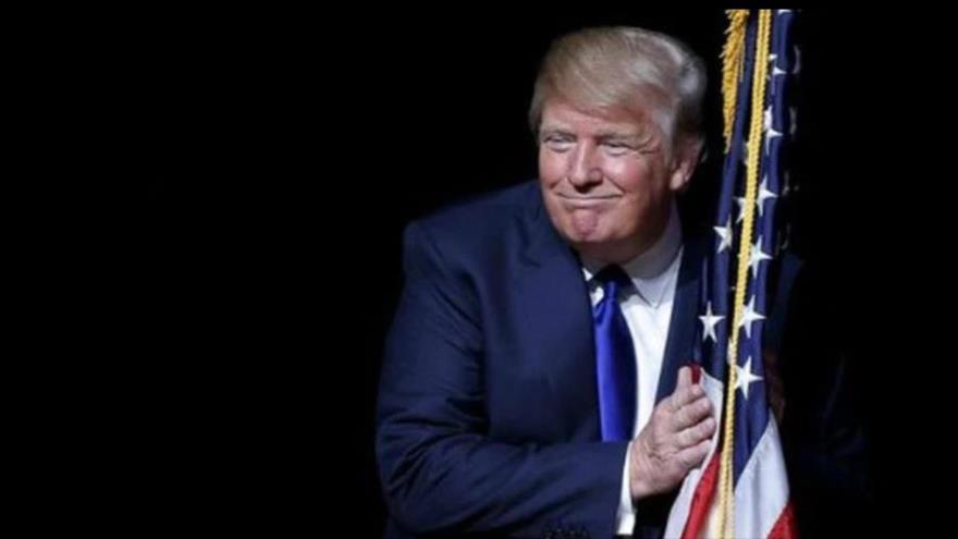 El presidente de EE.UU., Donald Trump, se arrima a una bandera nacional de Estados Unidos para frotarla con sus manos.