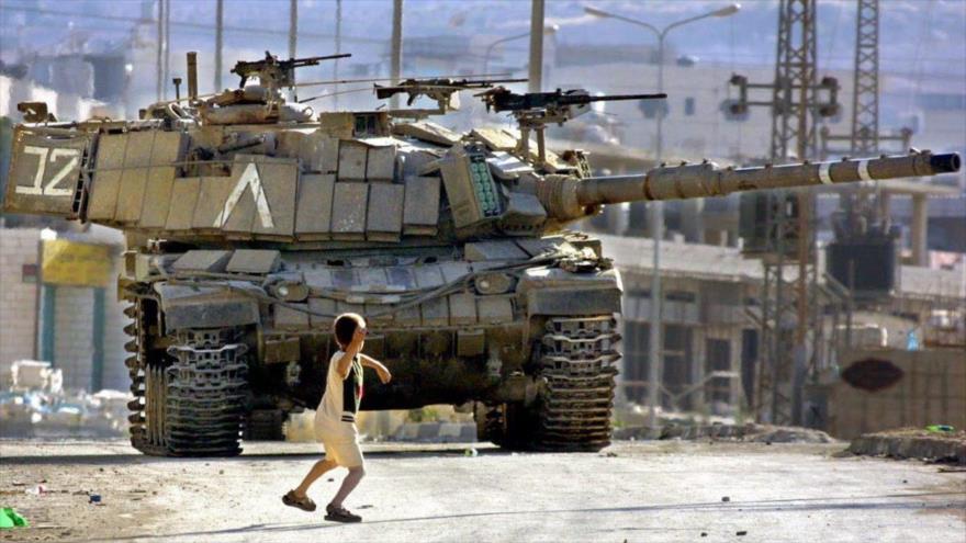 Un niño palestino lanza piedras contra un tanque israelí en la Cisjordania ocupada.