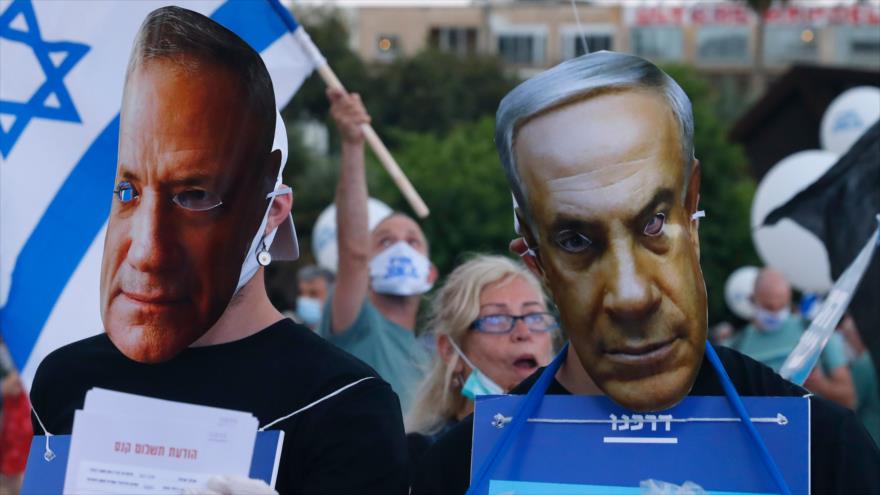 Manifestantes israelíes, con máscaras de Benjamín Netanyahu y Benny Gantz, protestan contra la anexión de Cisjordania, 23 de junio de 2020. (Foto: AFP)