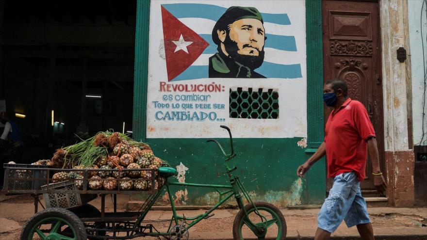 Un hombre cubano con mascarilla para evitar el contagio de la COVID-19, pasa junto a una imagen del difunto líder cubano Fidel Castro.