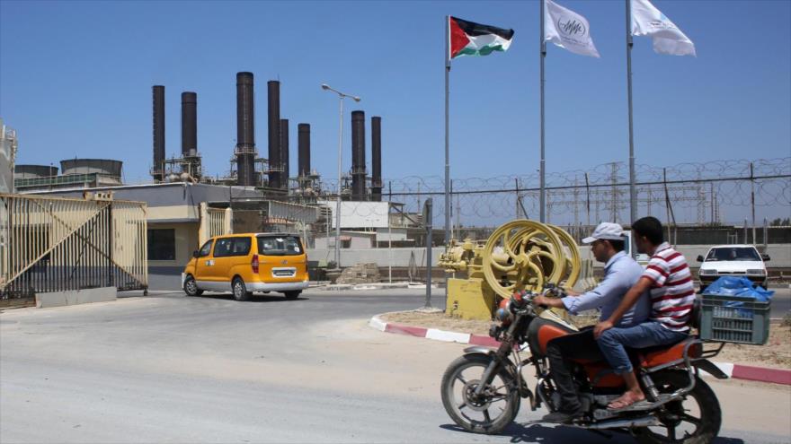 Dos en una motocicleta pasan frente a la central eléctrica de Gaza, en Nuseirat, centro de la Franja de Gaza. (Foto: AFP)