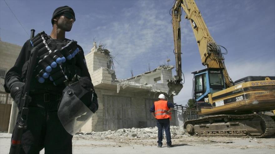 Un agente de policía israelí se encuentra cerca de una excavadora mientras derriba una casa palestina en la ciudad de Al-Quds, 7 de abril de 2009.