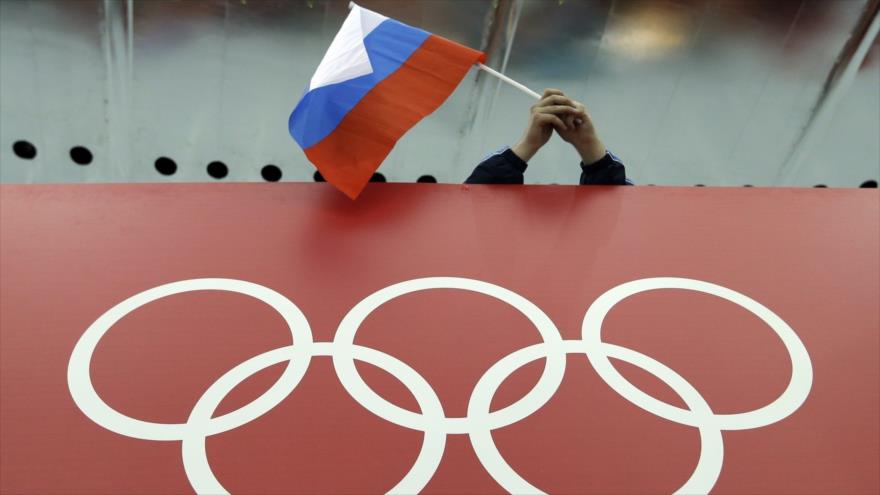 Una bandera rusa se sostiene sobre los anillos olímpicos durante los Juegos Olímpicos de Invierno en Sochi (Rusia), 18 de febrero de 2014. (Foto: AP).
