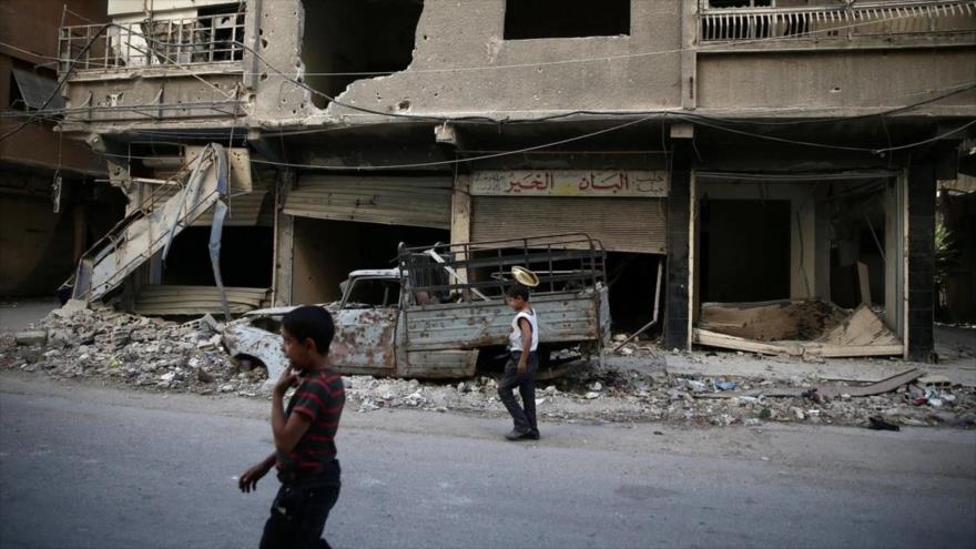 Niños caminan cerca de edificios dañados en Ain Tarma, suburbio de Damasco, capital siria. (Foto: Reuters)