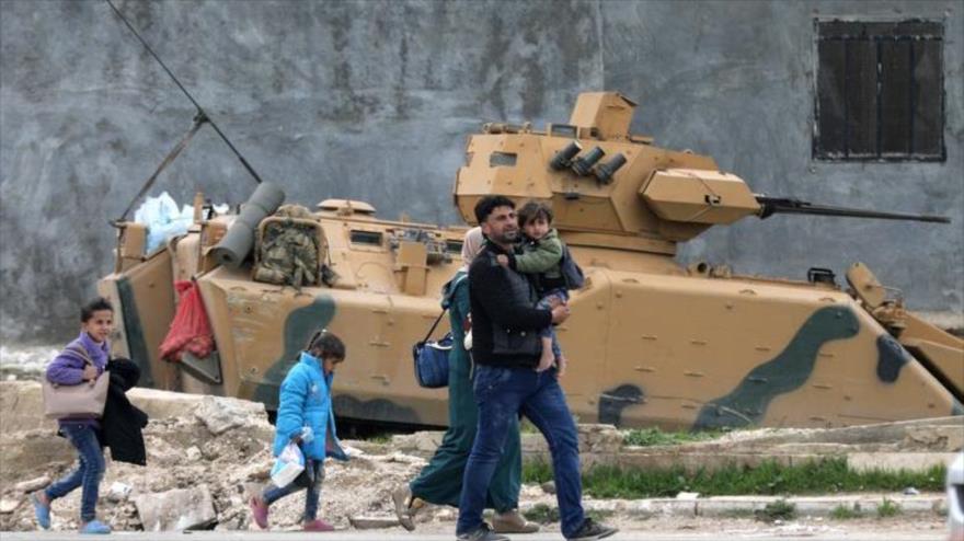 Familia pasa junto a un vehículo militar de los rebeldes sirios en el este de Afrin, marzo de 2018. (Reuters).