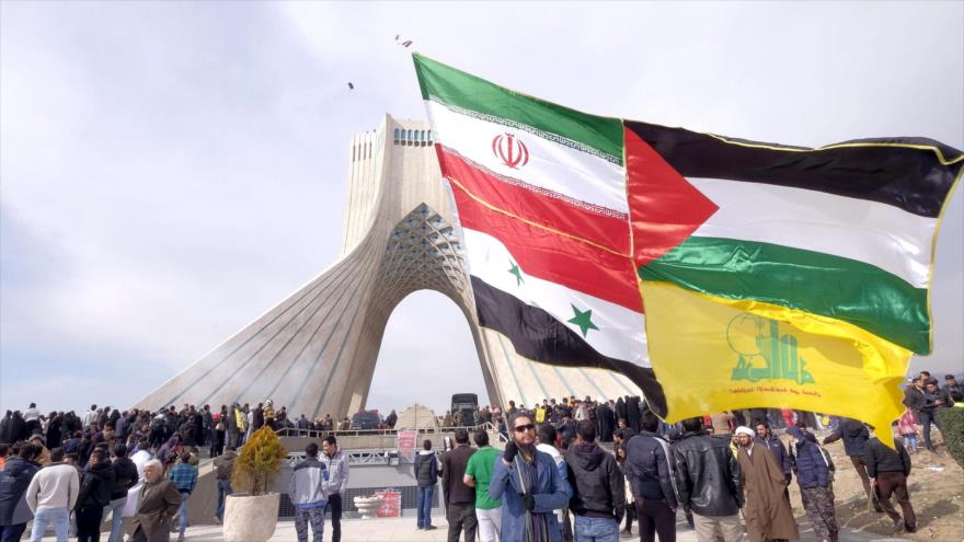 Un iraní sostiene las banderas de Irán, Palestina, Siria y el movimiento libanés Hezbolá durante la marcha por el aniversario de la Revolución Islámica de Irán.