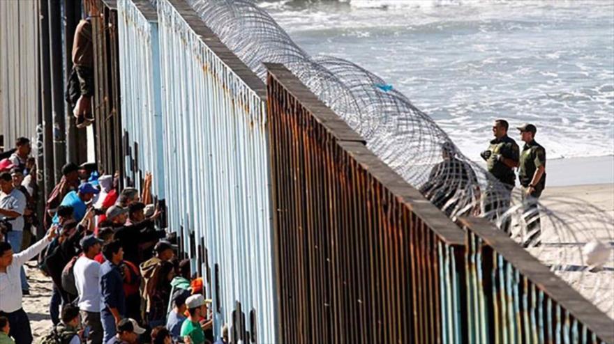 Un grupo de migrantes aguarda detrás de la verja de Tijuana en el lado mexicano de la frontera con EE.UU.