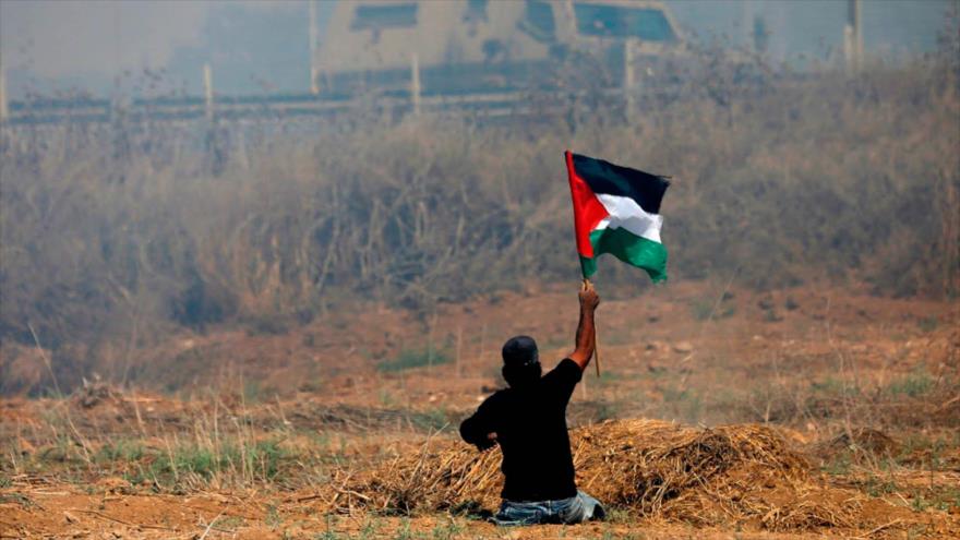 Un palestino muestra la bandera de Palestina durante confrontaciones con soldados israelíes, Gaza, 19 de mayo de 2017. (Foto: AFP)