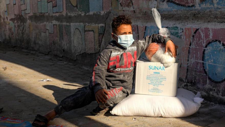 Un niño palestino sentado junto a paquetes de ayuda humanitaria en la Franja de Gaza, 31 de enero de 2021. (Foto: AFP)
