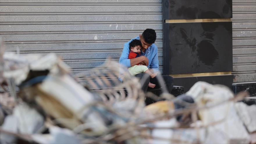 Un padre palestino y su hijo están sentados frente a su casa destruida en un ataque israelí a Gaza, 16 de mayo de 2021. (Foto: AFP)